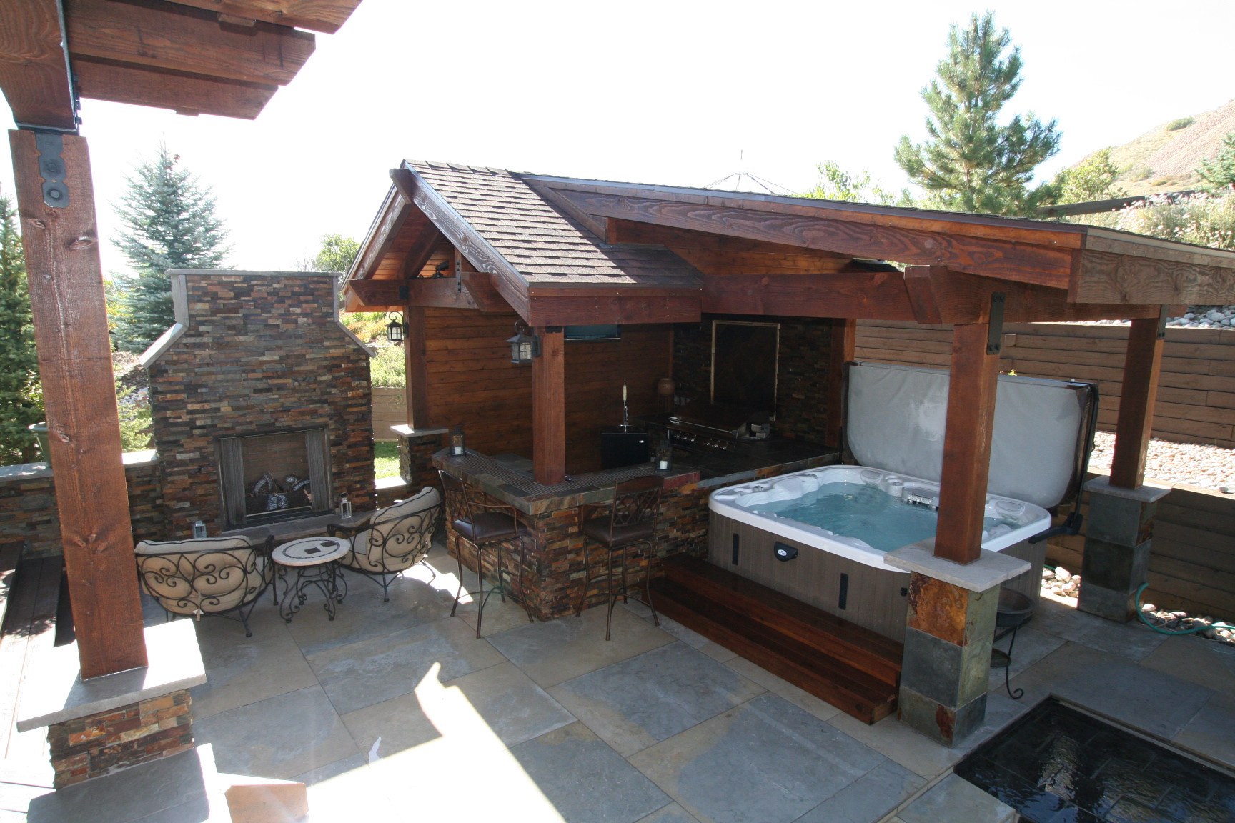 Custom outdoor living area with timber pavilion, stone fireplace and hot tub